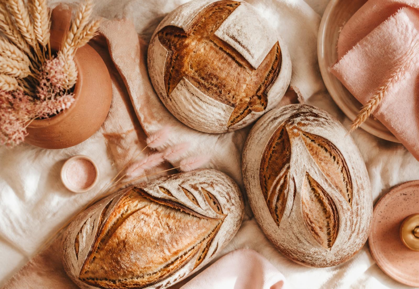 Three scored sourdough loaves resting on cream linen with blush pink and terracotta props